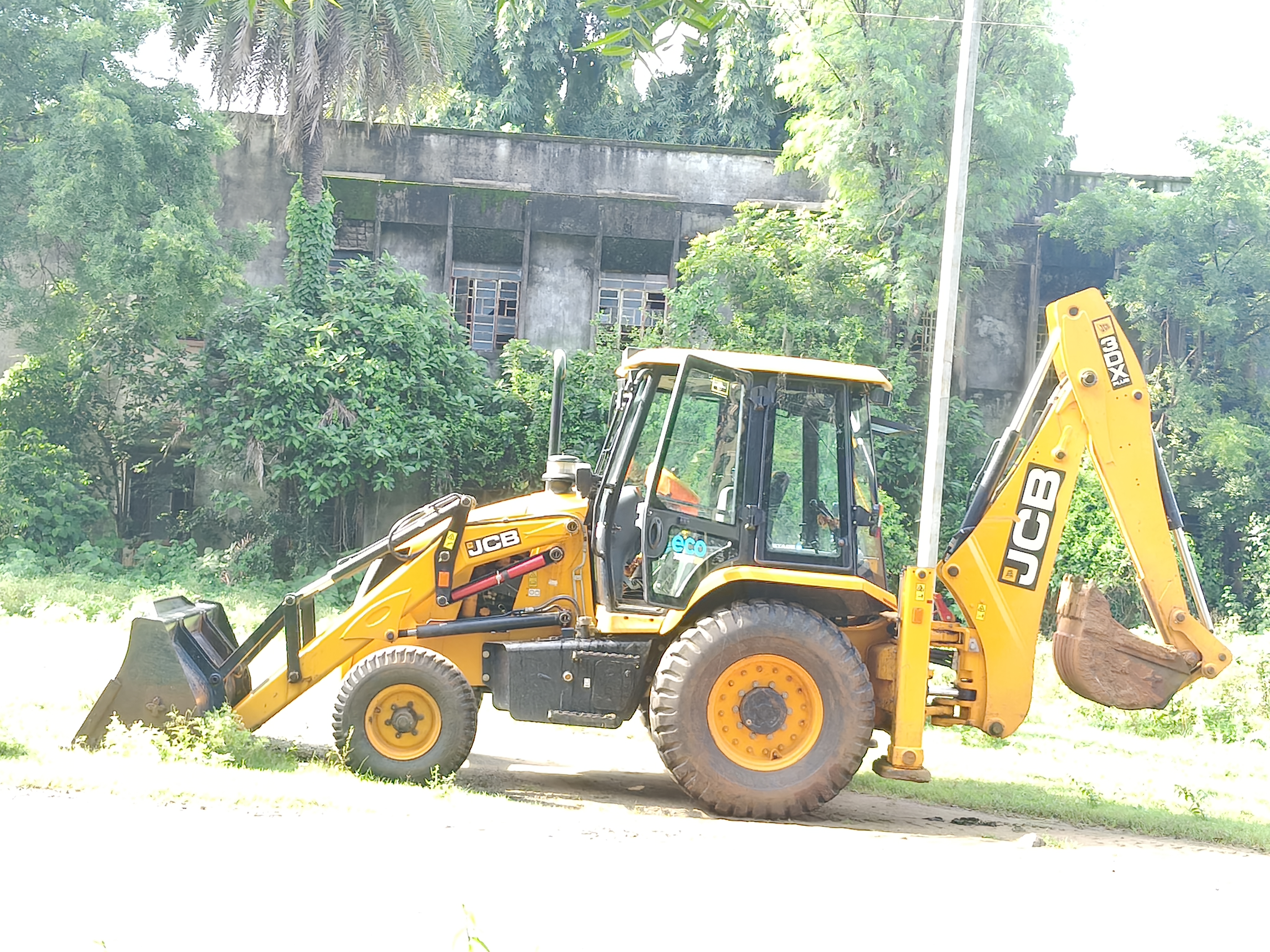 A yellow backhoe loader parked outdoors near green trees."